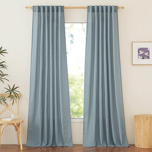 Dusty blue linen blend tab top curtains hanging on a wooden rod by a bright window.