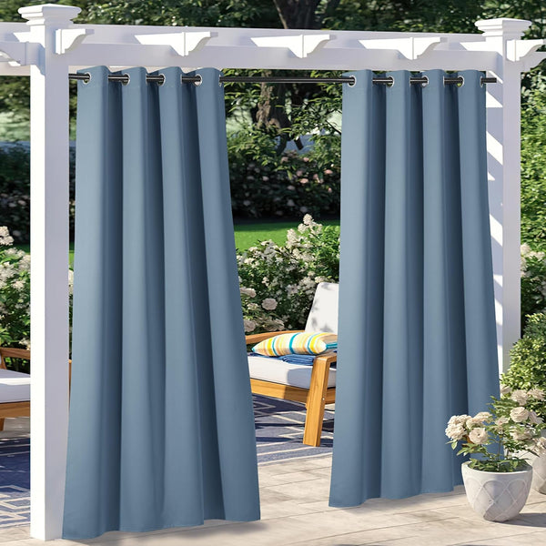 Dusty blue grommet top outdoor curtains hanging on a white pergola on a sunny patio.