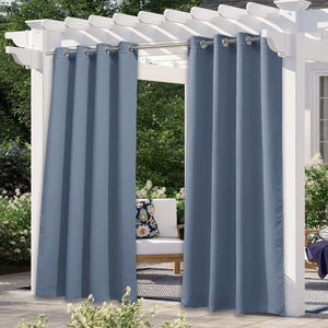 Dusty blue outdoor curtains with silver grommets hanging from a white pergola on a sunny patio.