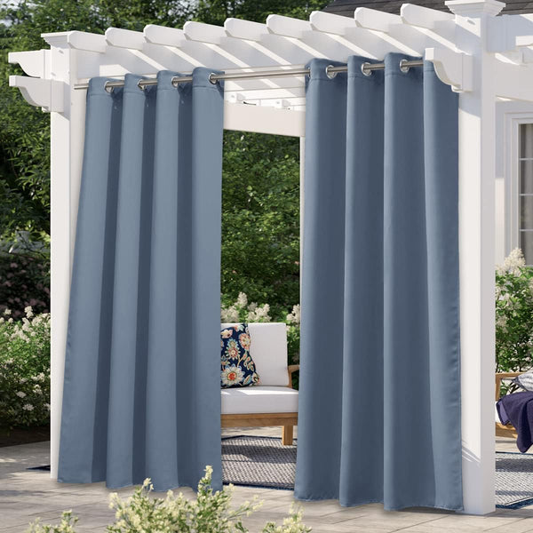 Dusty blue outdoor curtains with silver grommets hanging from a white pergola on a sunny patio.