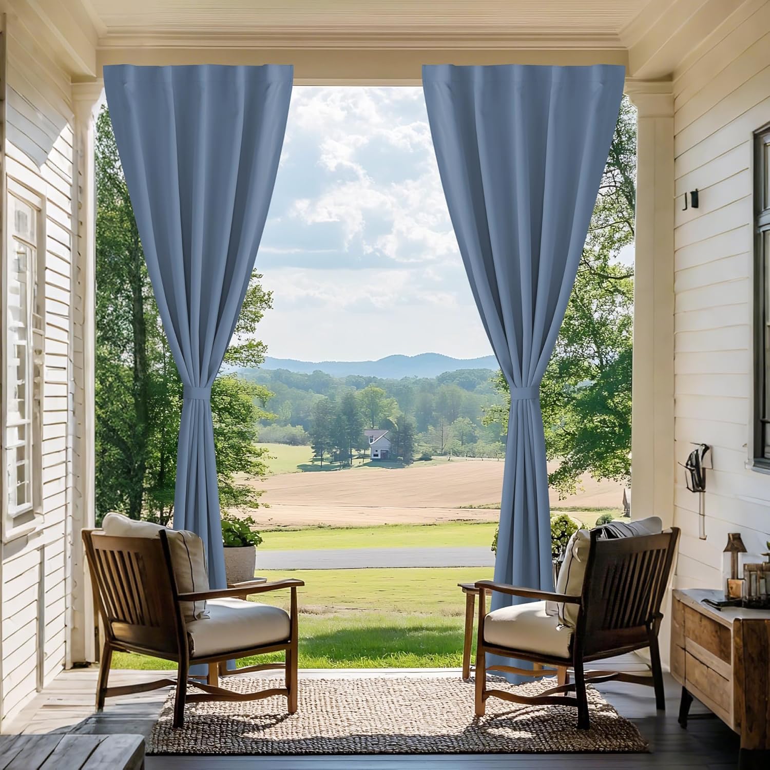 Dusty blue outdoor curtains with tiebacks, hanging on a porch framing a scenic view.
