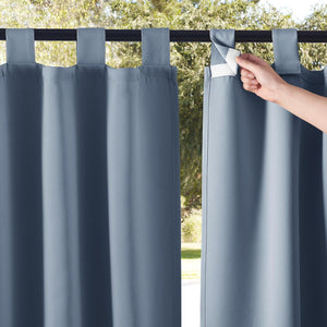 Dusty blue outdoor curtains with hook-and-loop tab tops. Hand securing one on a rod, green view.