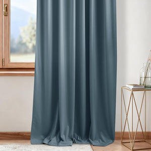 Smooth dusty blue blackout curtain panel hanging beside a wooden window.