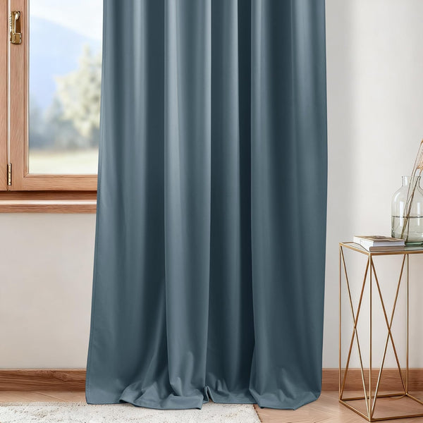 Smooth dusty blue blackout curtain panel hanging beside a wooden window.