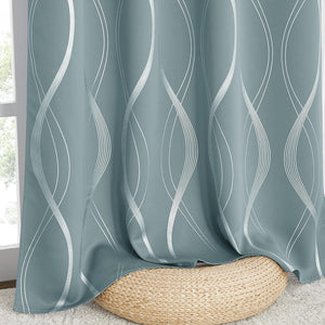 Dusty blue blackout curtain with modern white wavy abstract pattern, gracefully drapes over a woven straw pouf near a window.