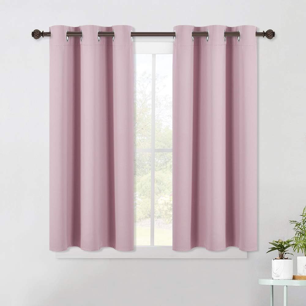 Pair of dusty pink blackout curtains with silver grommets hanging on a dark rod over a window.