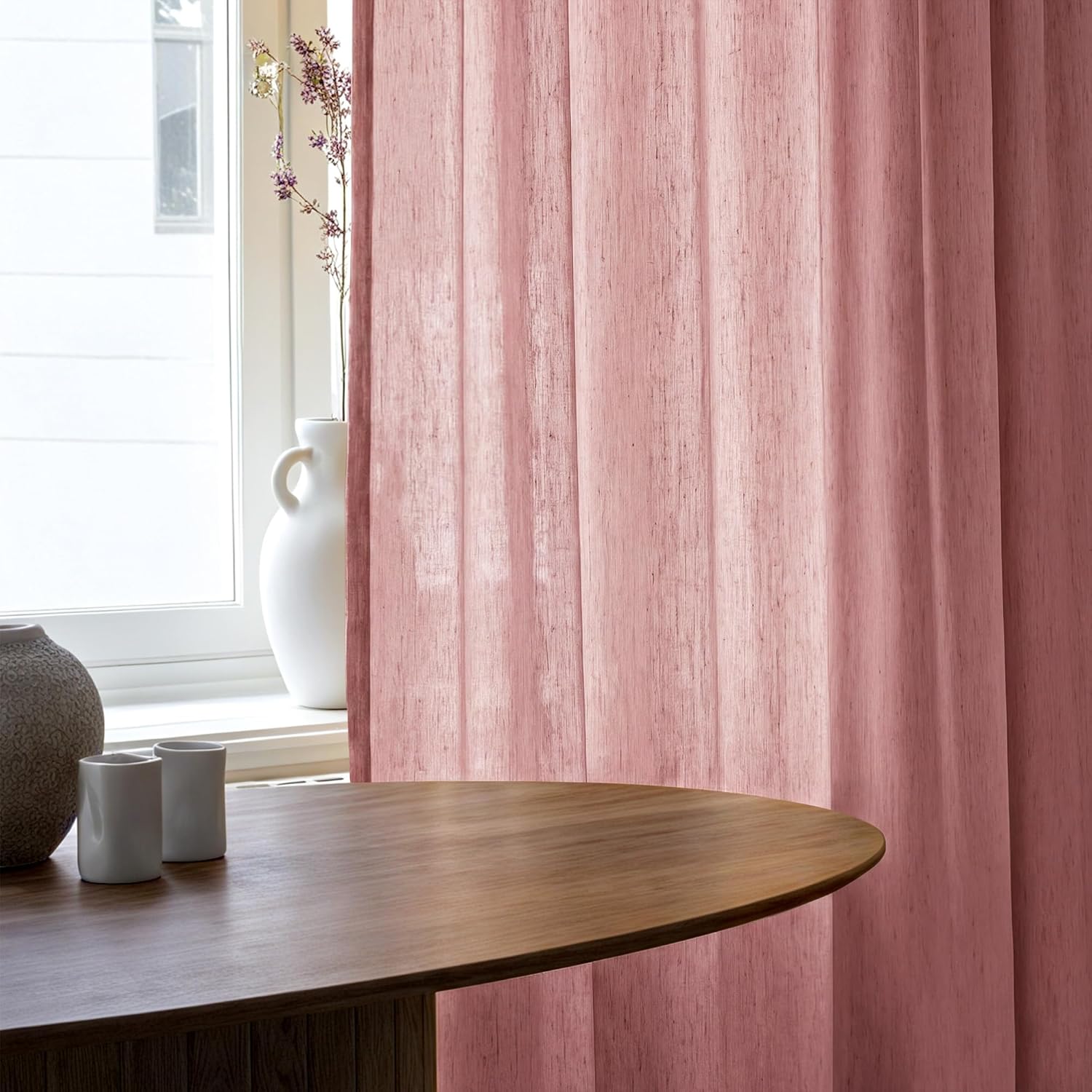 Dusty pink linen-look vertical panel curtains with visible texture next to a bright window.