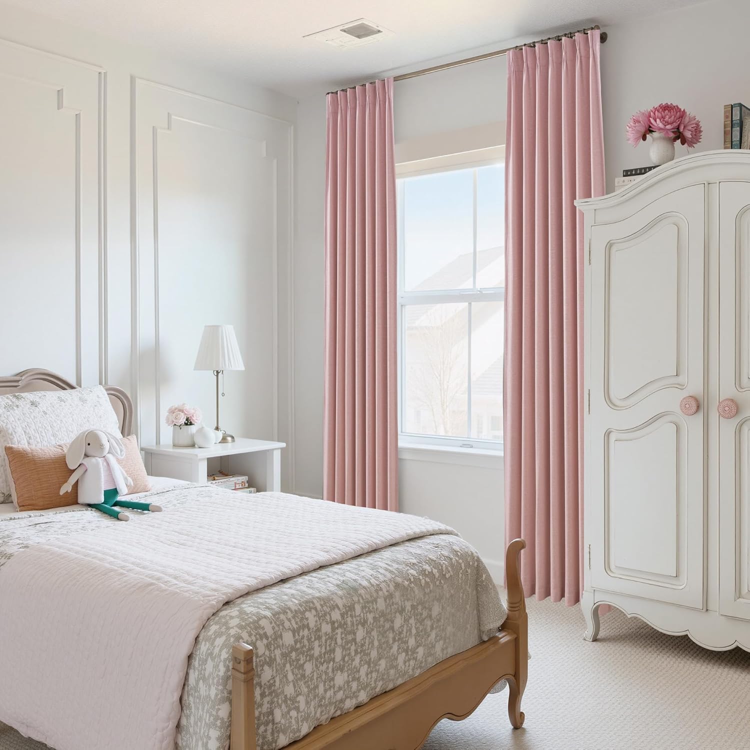 Dusty pink pleated curtains frame a window in a cozy bedroom with a white bed and ornate wardrobe.