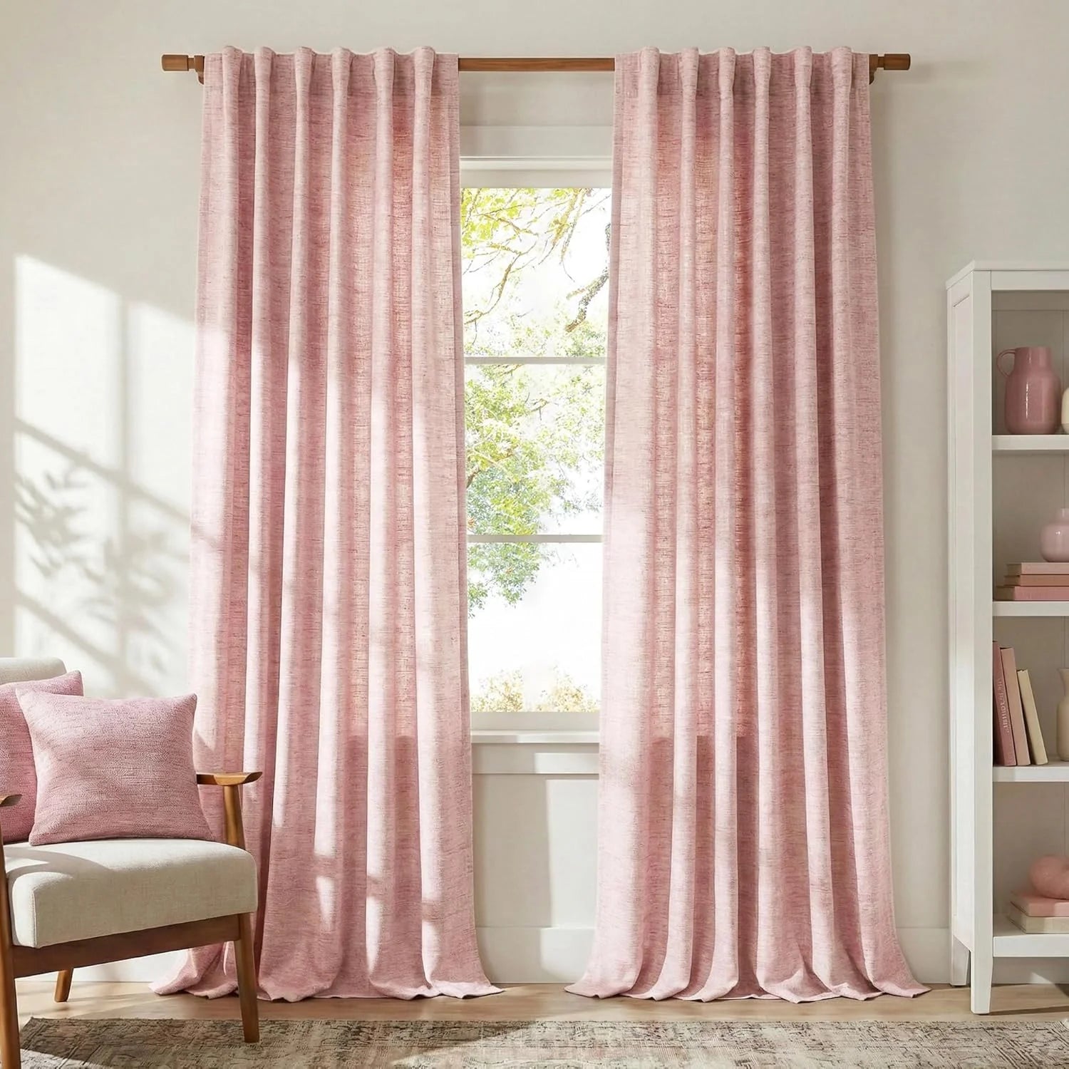 Pair of blush pink textured curtains hanging on a wooden rod by a large window in a bright living room.