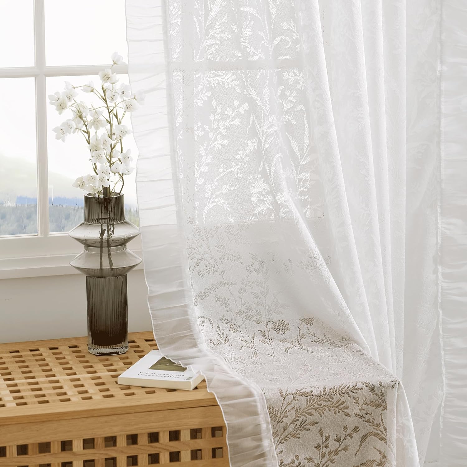 White sheer curtain featuring a subtle floral damask pattern and elegant ruffled trim, brightening a window.