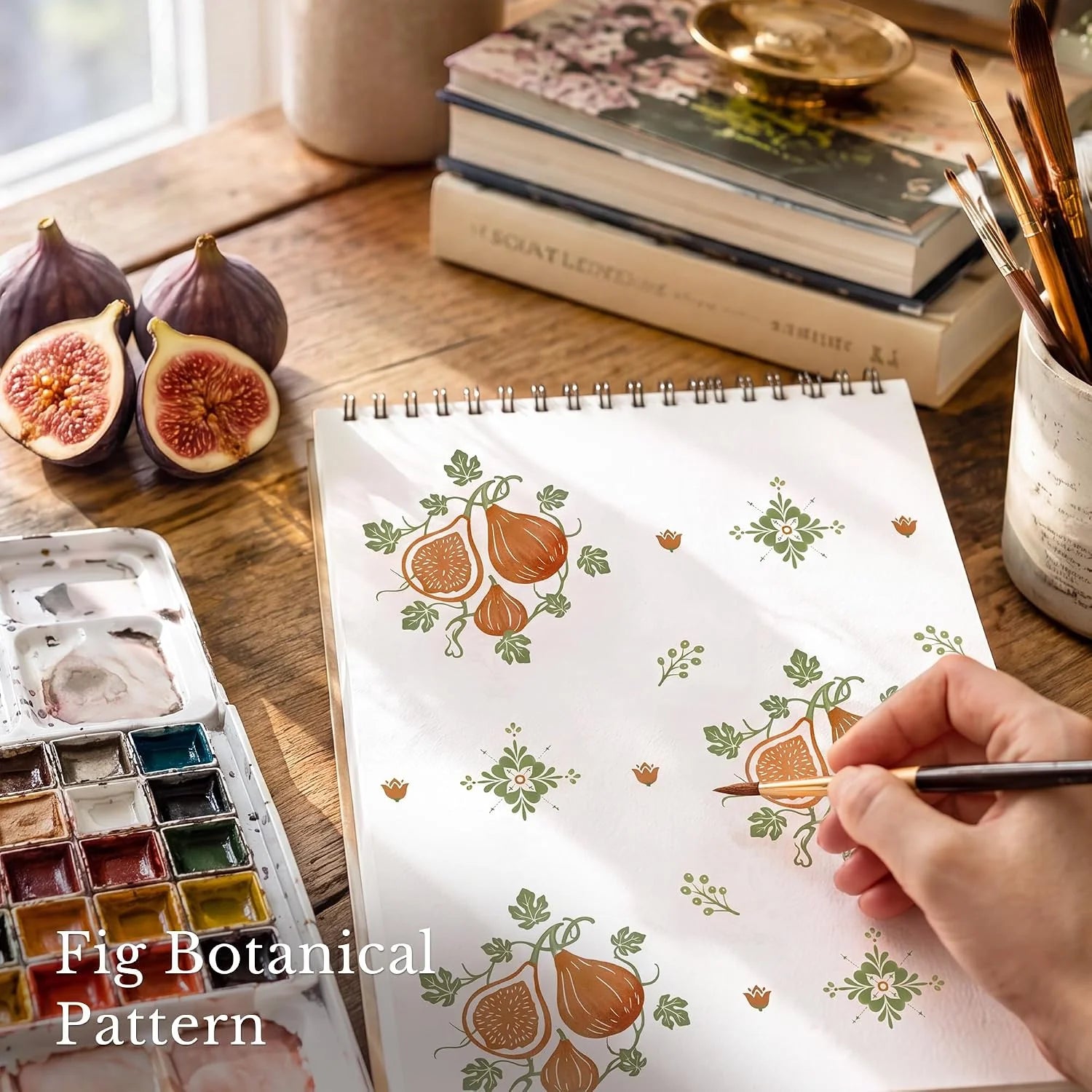 Hand painting a fig botanical pattern in a sketchbook on a wooden desk