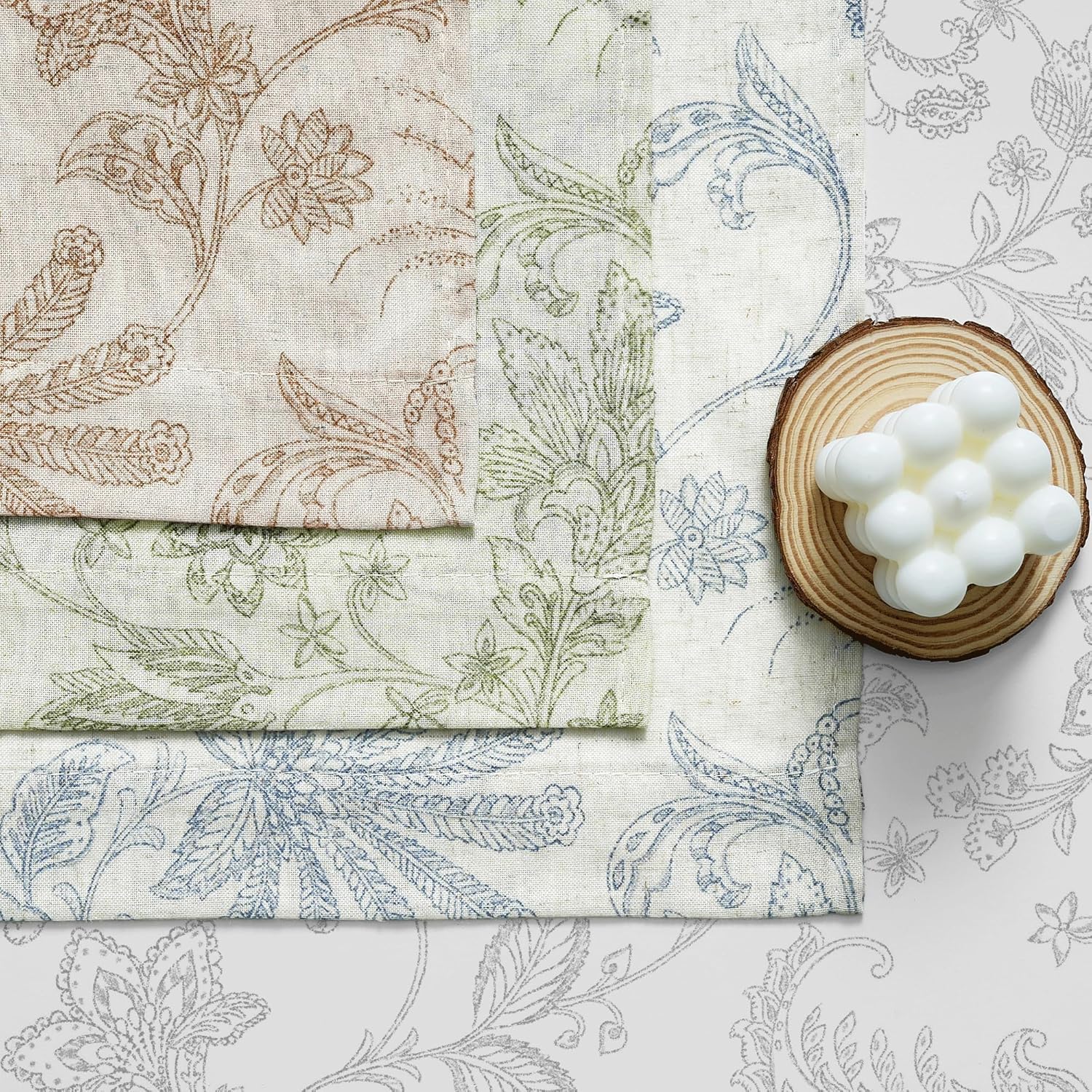 Stacked linen-look fabric swatches in brown, green, and blue floral patterns.