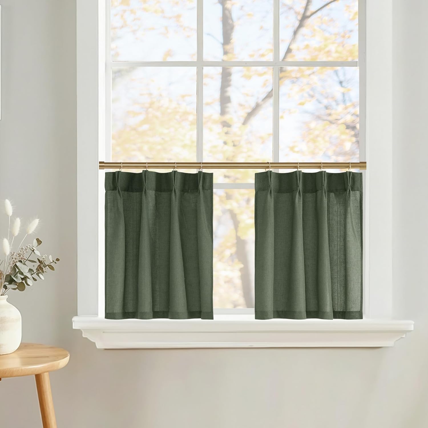 Two forest green linen-look cafe curtains on a gold rod filtering light in a sunny window.