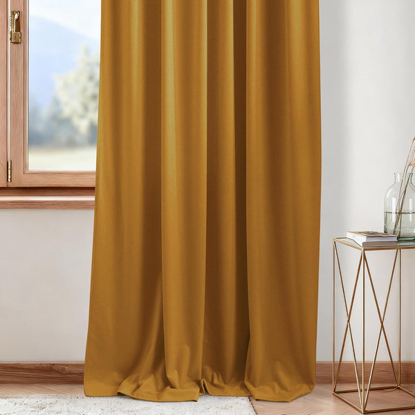 Elegant golden yellow velvet curtain panel drapes gracefully, pooling on the floor next to a wooden window frame.
