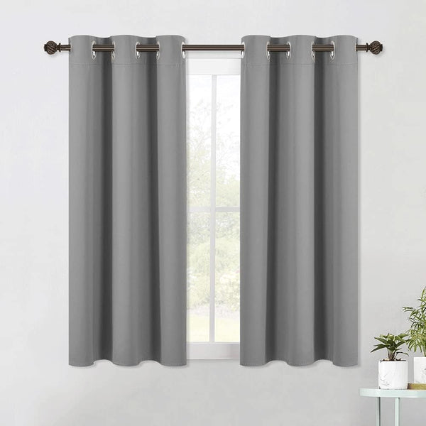 Pair of gray blackout curtains with silver grommet tops hanging on a dark metal rod over a window.