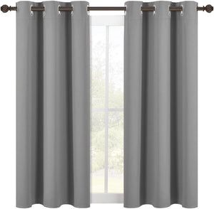 Two solid gray blackout curtain panels with silver grommets hang on a dark bronze rod in front of a window.
