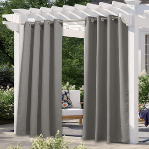 Two dark gray outdoor patio curtains with silver grommets hang from a white pergola, offering privacy.