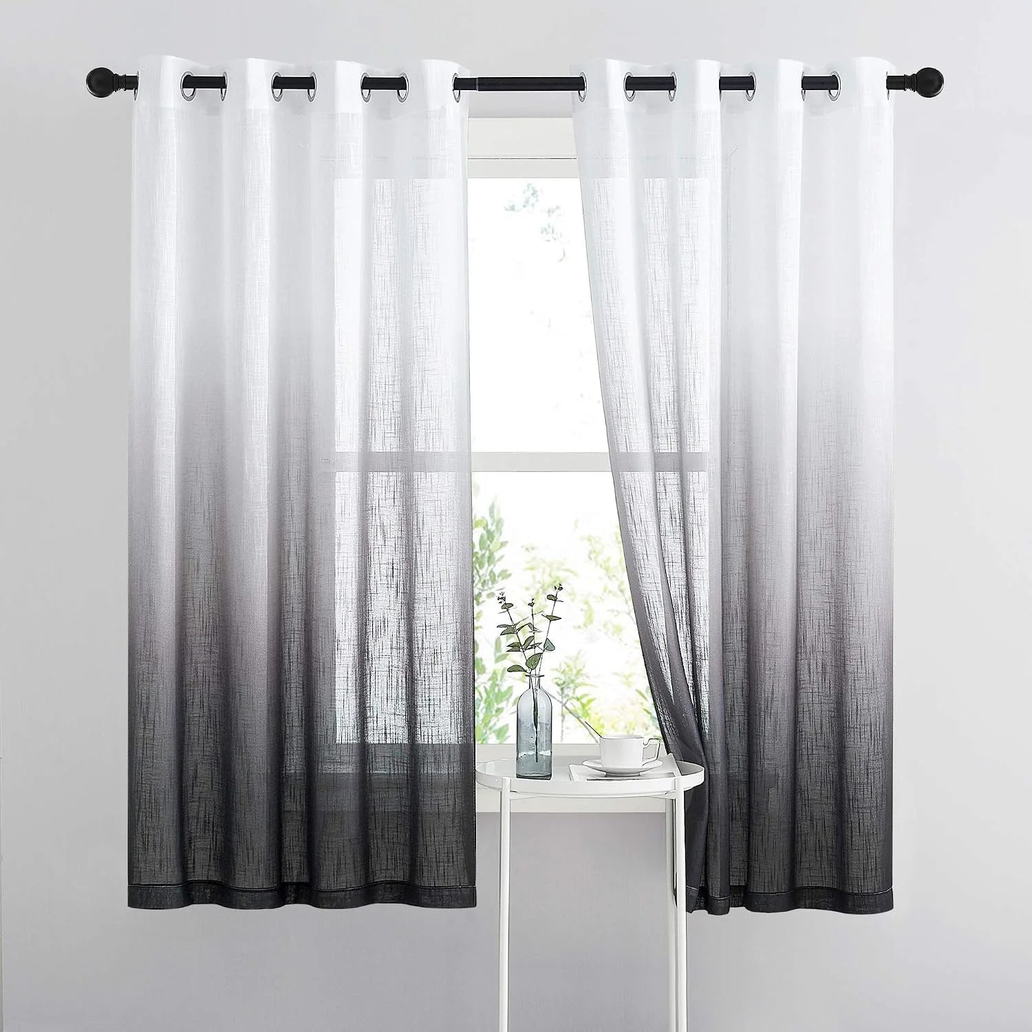 Gray ombre sheer curtains with silver grommets hanging on a black rod by a bright window
