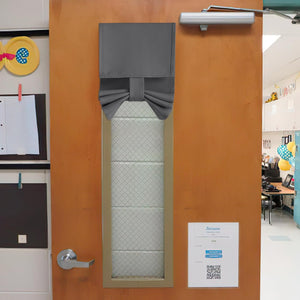 Gray fabric Roman blackout shade cinched in the middle, covering a wired glass window on a wooden classroom door.