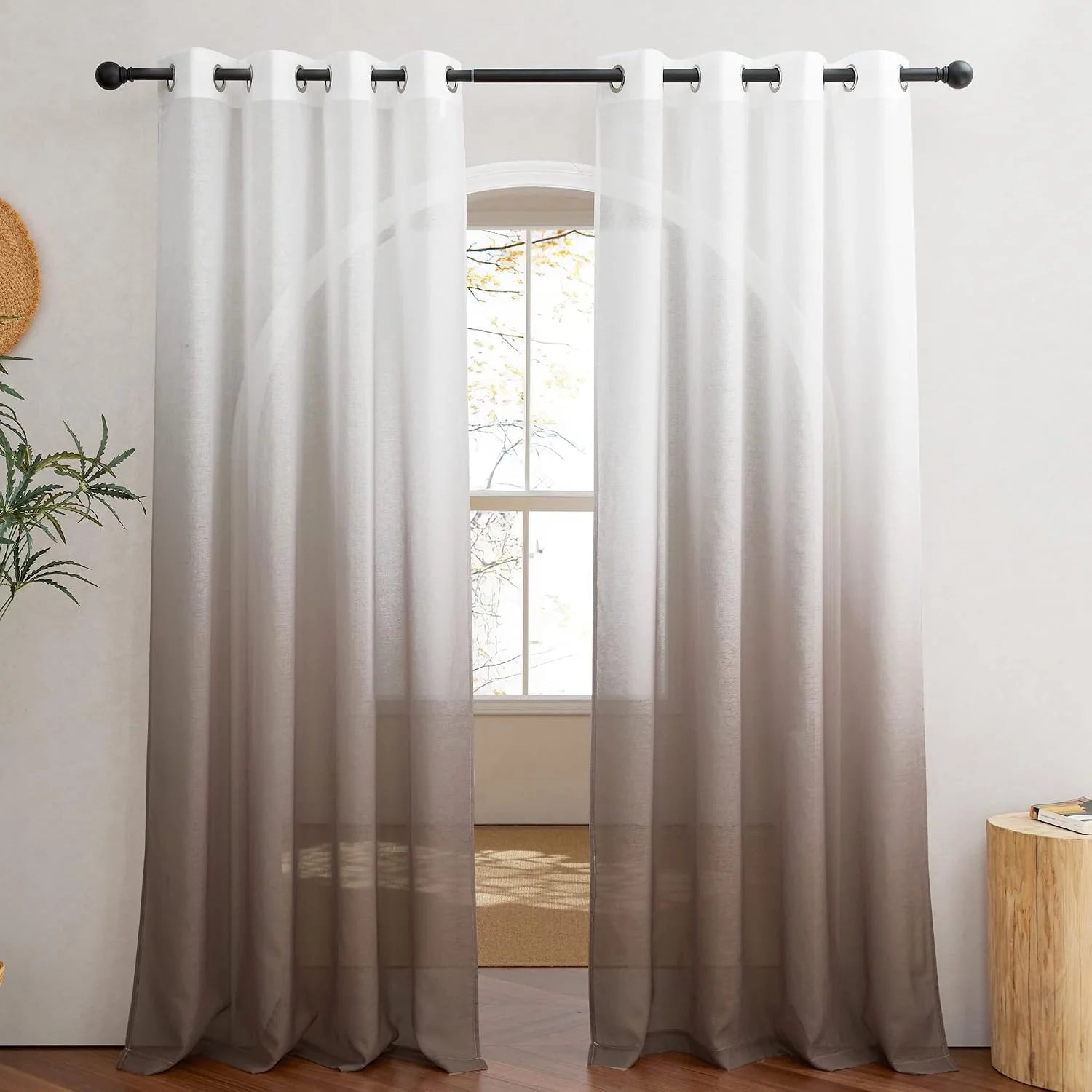 Gray ombre sheer curtains with silver grommets hanging on a black rod by a bright window