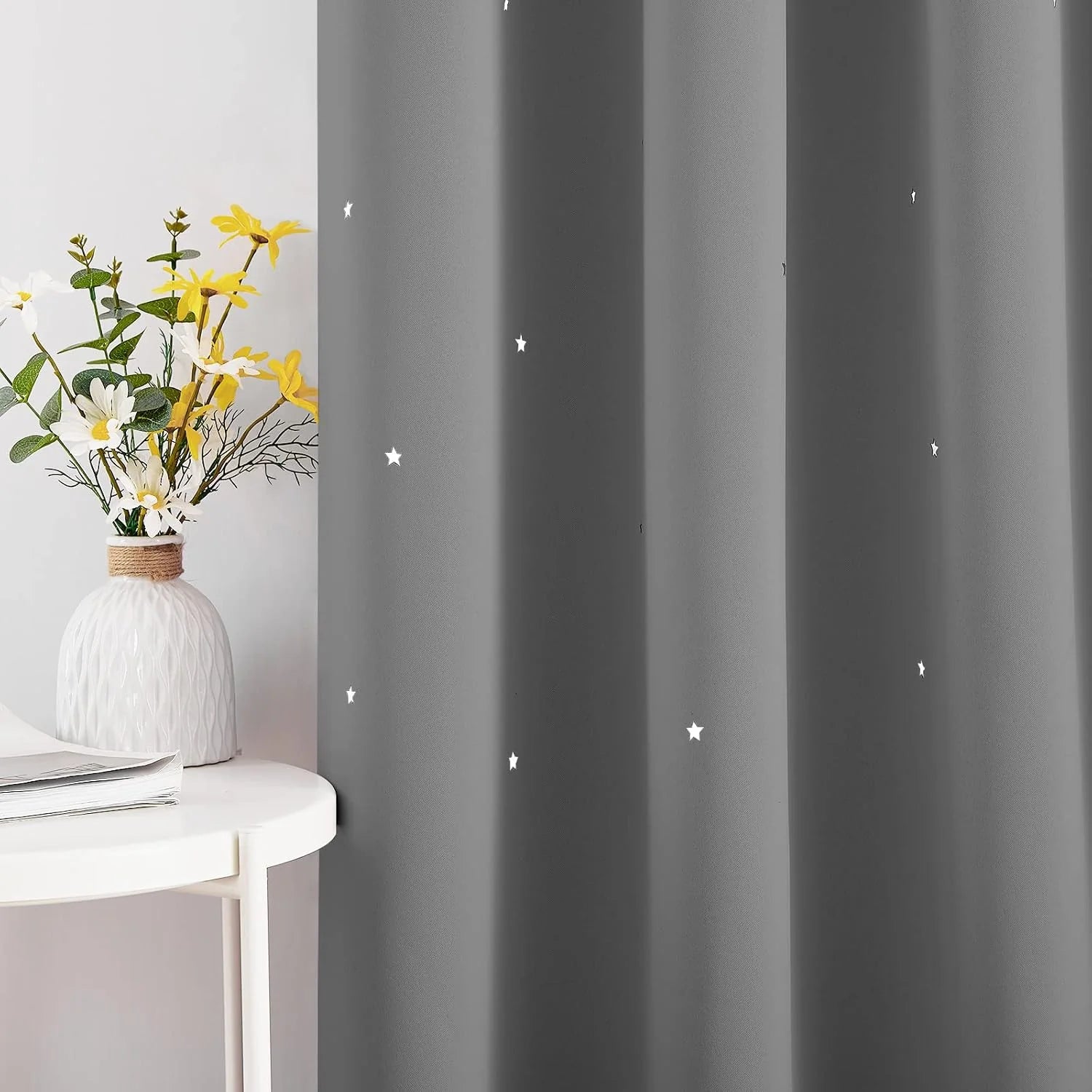 Gray blackout curtain with small white star pattern beside a white side table and vase