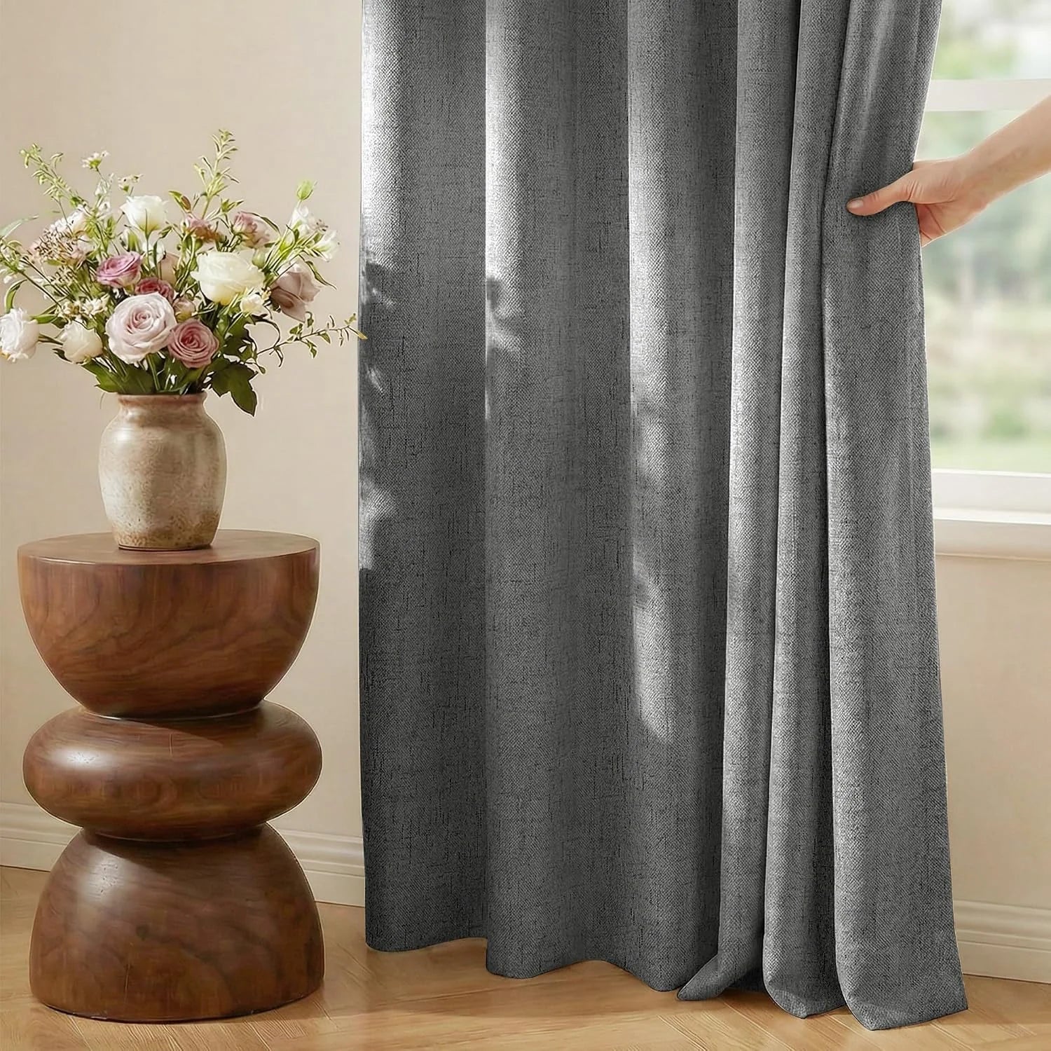 Gray textured curtain panel by a bright window beside a wooden side table with flowers