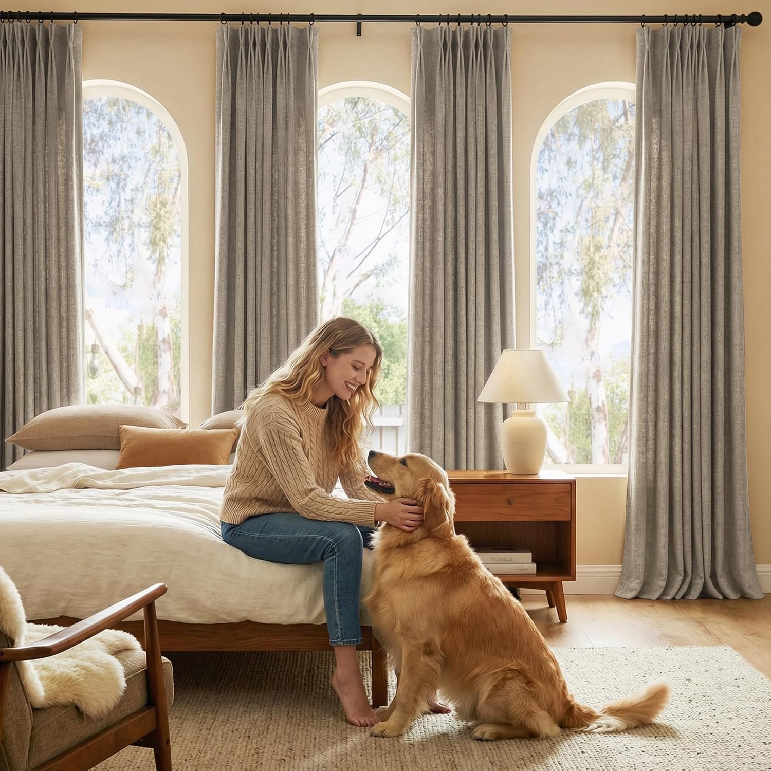 Textured light gray pinch pleat curtains hang elegantly on black rods over arched bedroom windows.
