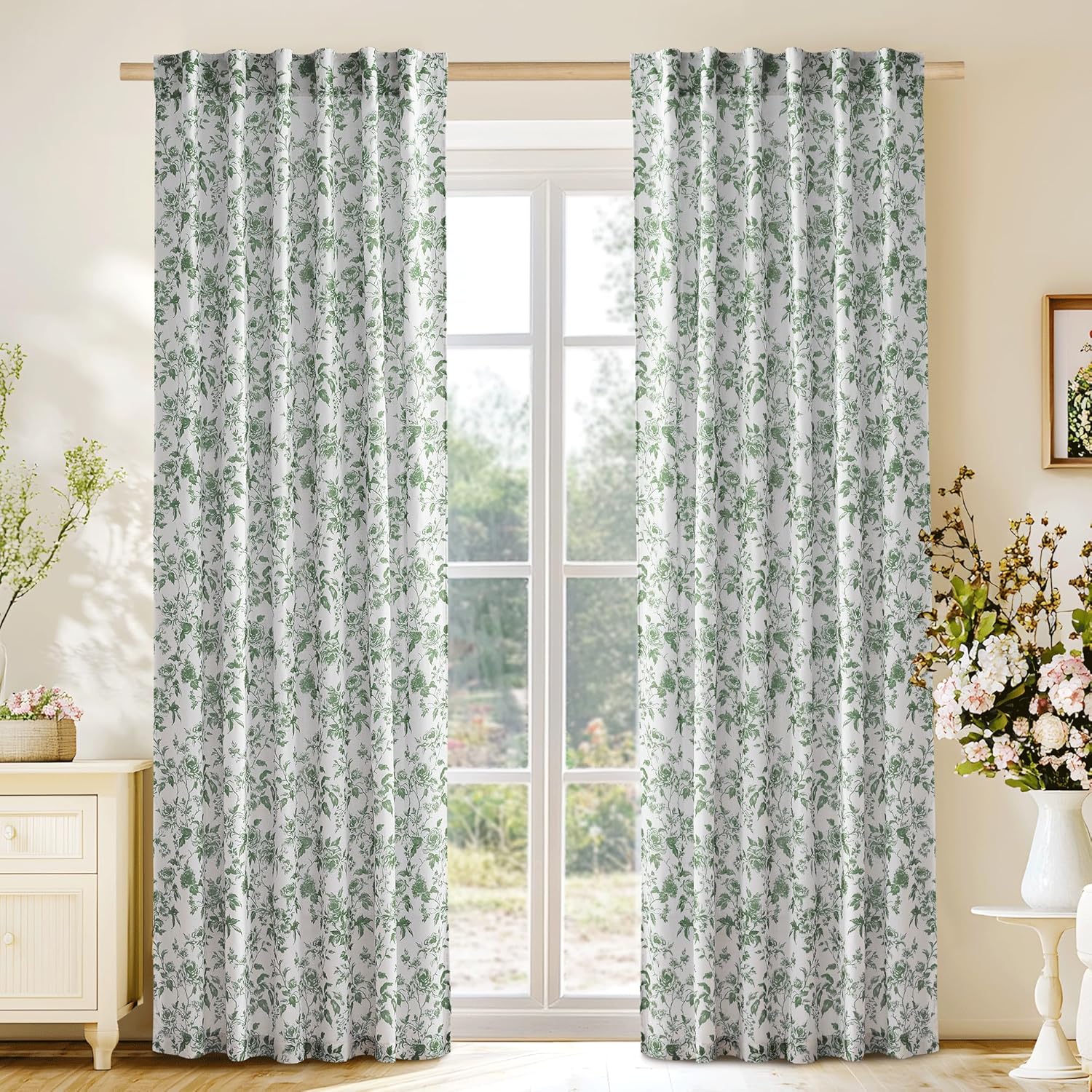 Pair of white curtains with delicate green botanical floral print and pleated top on wooden rod.