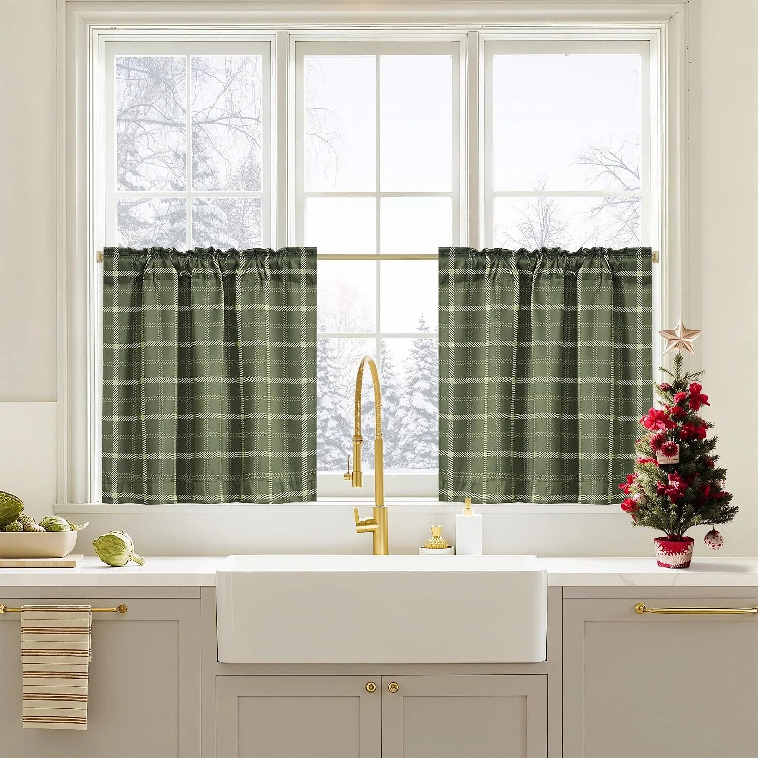 Green plaid tier curtains over a kitchen sink window with brass faucet and holiday decor