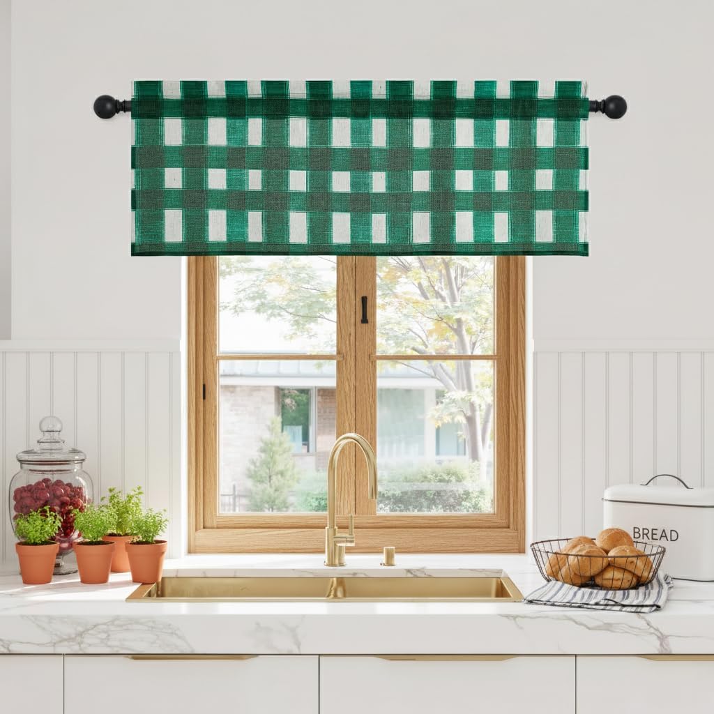 Green and white gingham pattern window valance hangs over a kitchen sink with a brass faucet.