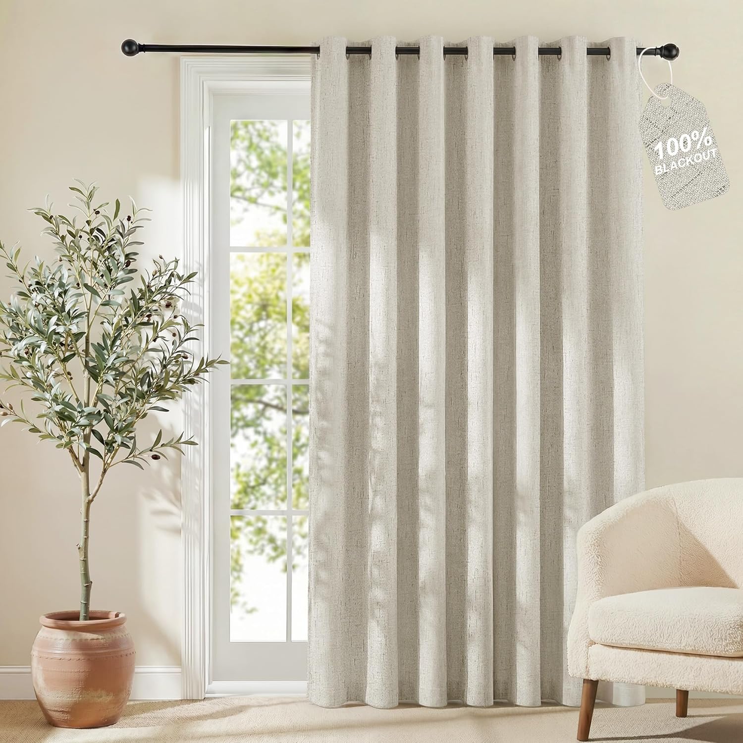Greige textured 100% blackout curtain with black grommets, hanging on a rod by a window.