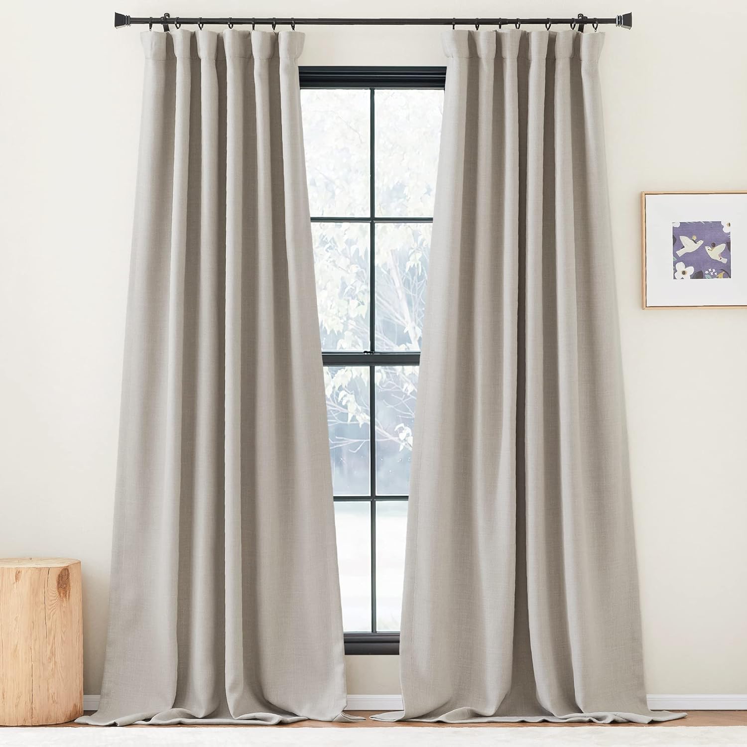 Greige linen-blend curtains with tailored pleat top, hung on black rod, pooling on light rug.