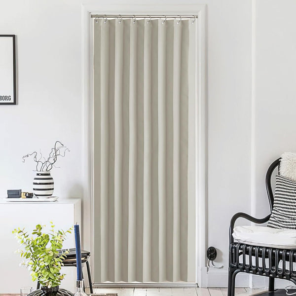 Full-length greige pleated blackout doorway curtain with metal rings, providing privacy in a white-walled room.