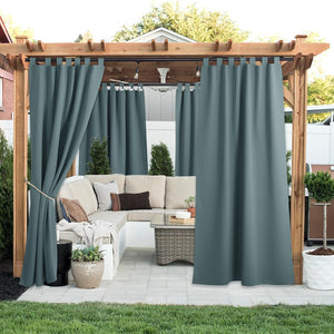 Grey-blue tab top outdoor patio curtains hanging from a wooden pergola over a cushioned sofa.