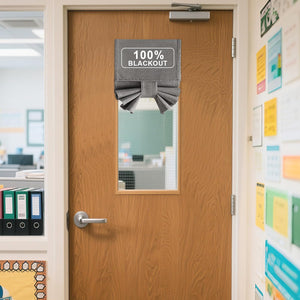 Grey fabric door window shade with '100% BLACKOUT' label, covering a glass panel on a wooden office door.