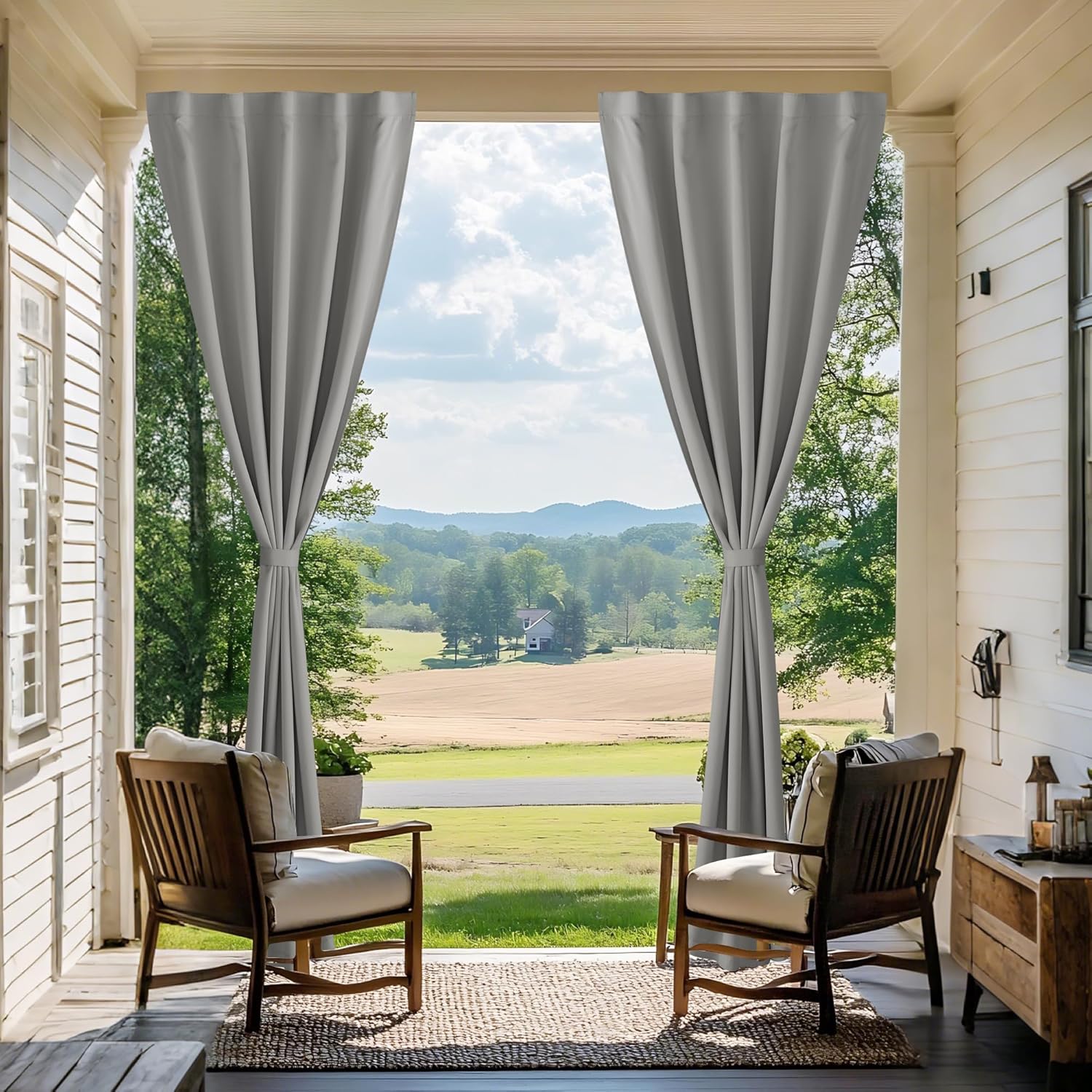 Grey outdoor patio curtains tied back on a rustic porch, overlooking green fields and hills.