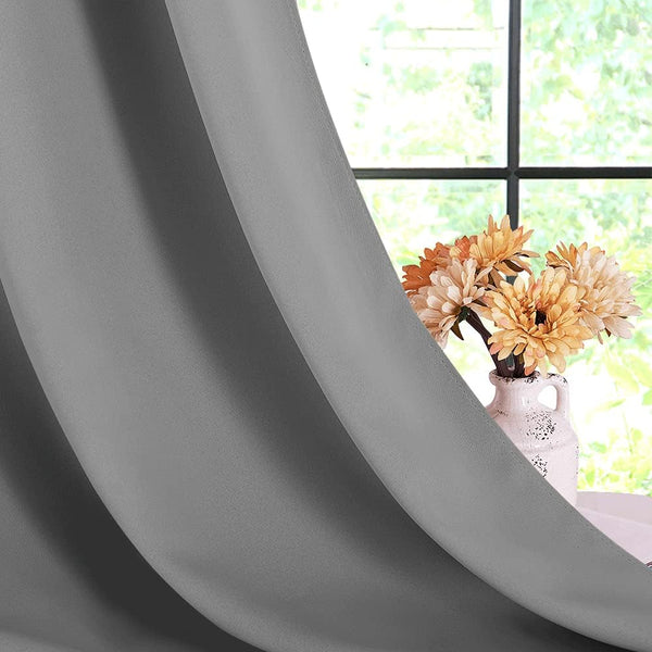 Smooth grey room darkening curtain panel with soft drapes, partially covering a window with a vase of orange flowers.