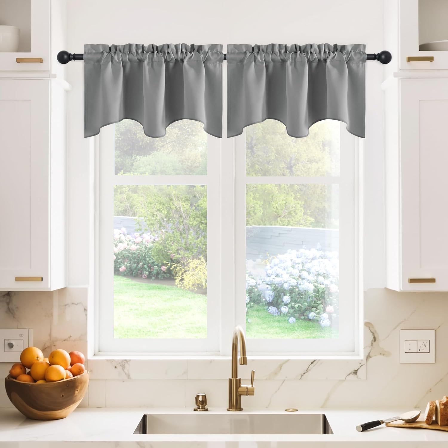 Grey scalloped valance curtain with a gathered rod pocket top, covering a kitchen window above a sink.