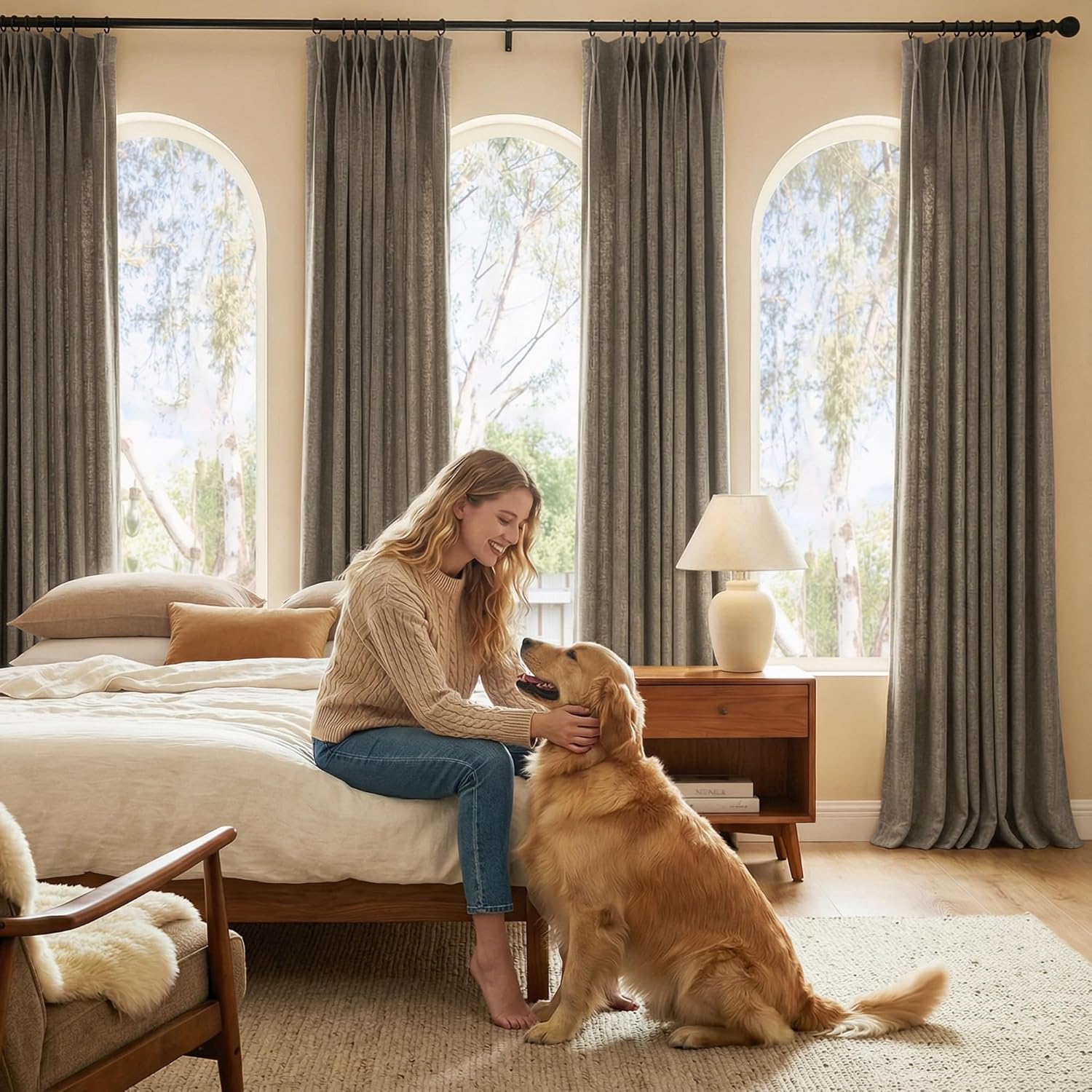 Textured grey pinch pleat drapes hung on a black rod over arched windows in a cozy bedroom.