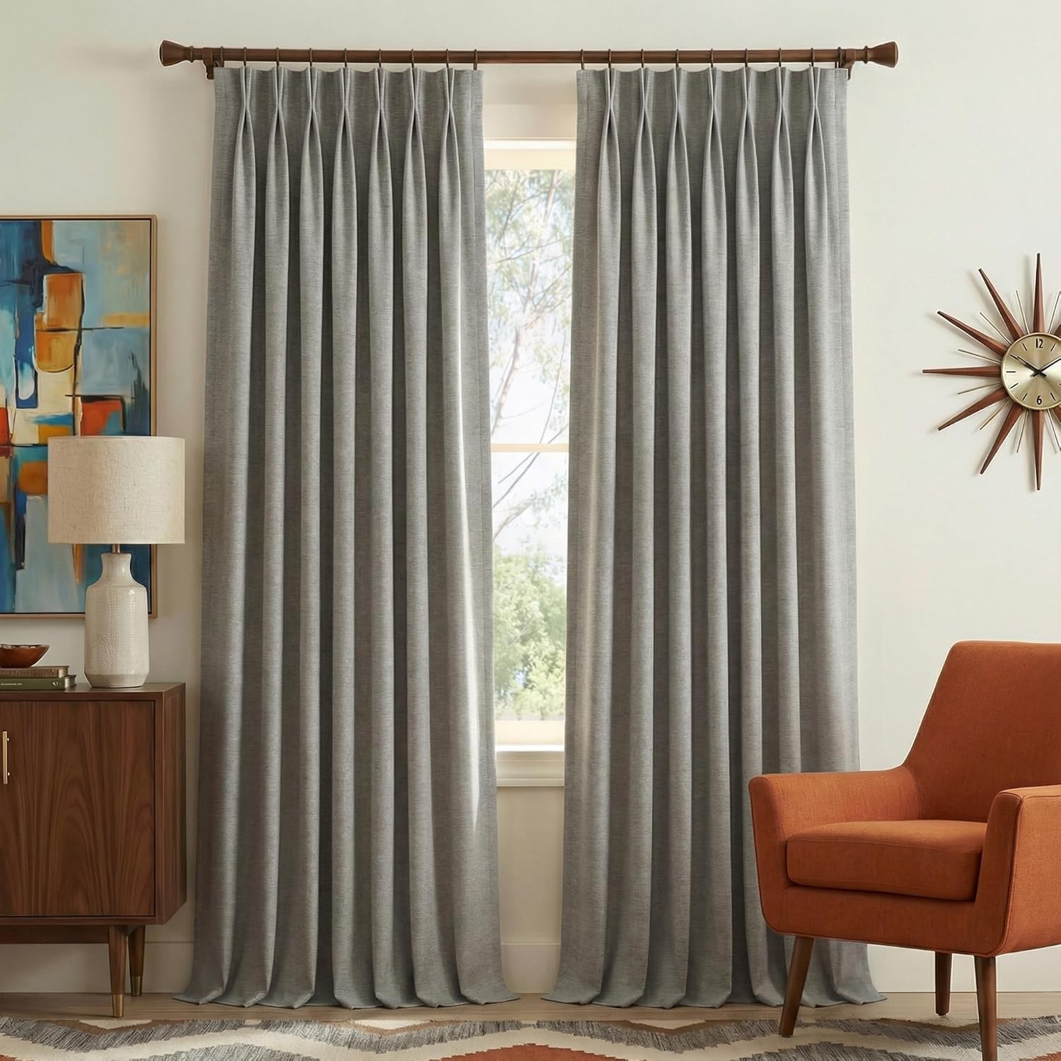 Pair of light grey textured pinch pleat curtains on a dark wooden rod framing a bright window.