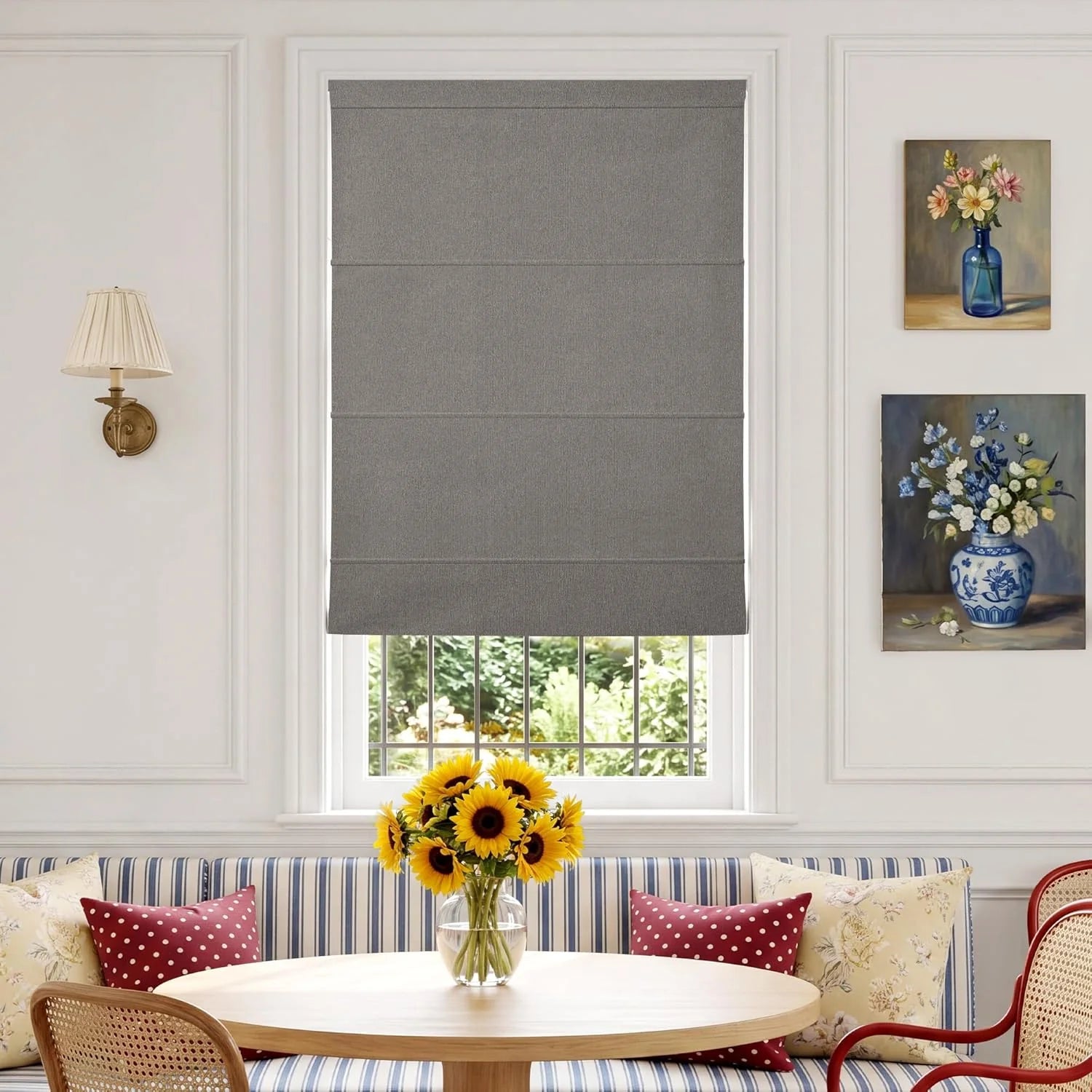 Grey textured fabric Roman shades in a bright dining nook with a striped banquette and sunflowers on the table.