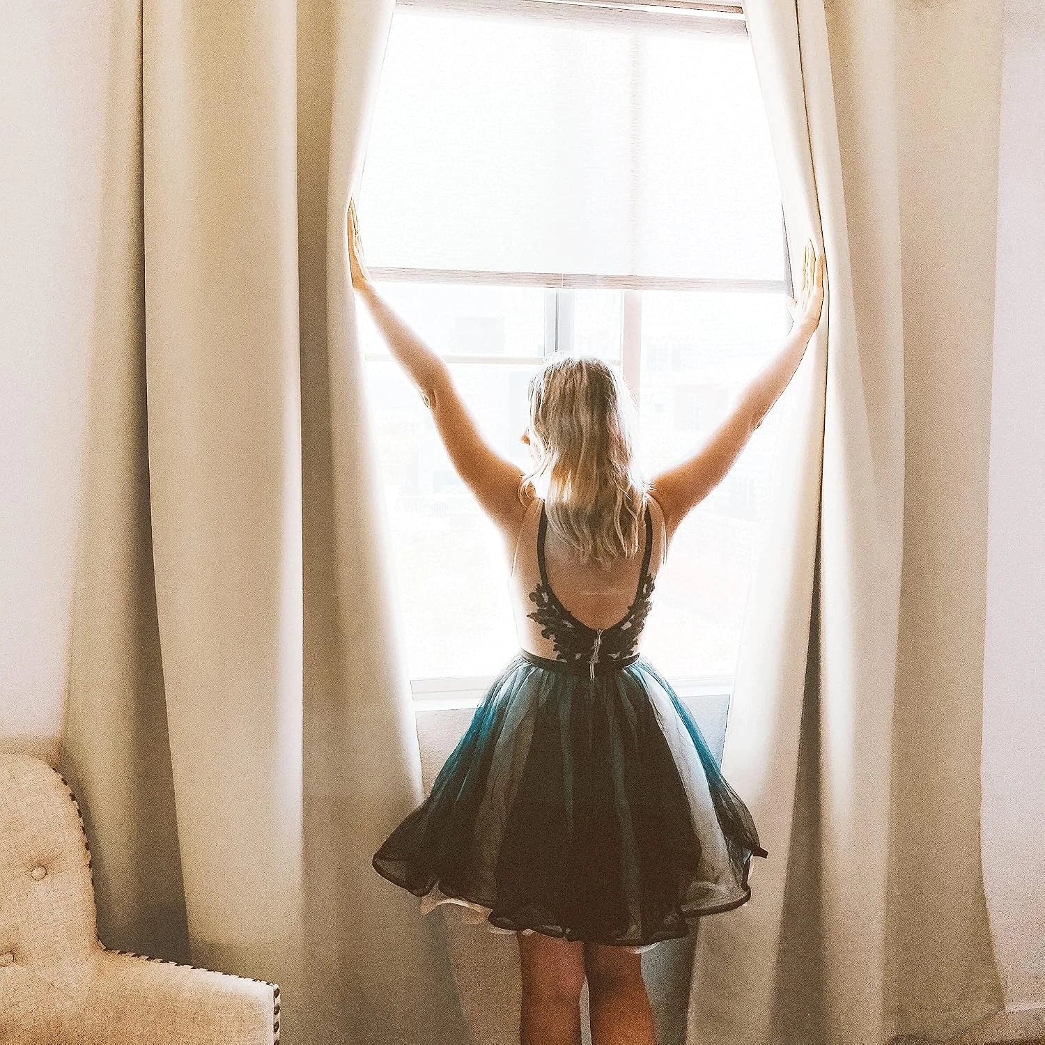 Woman opening ivory blackout curtains at a bright bedroom window