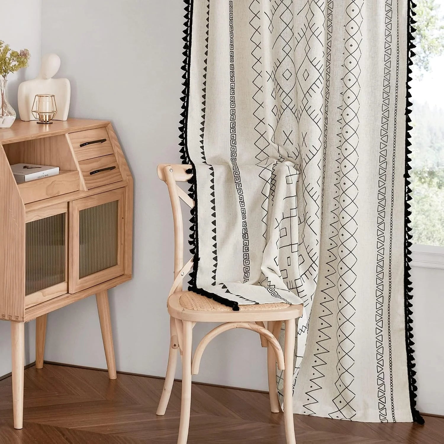 Ivory boho curtain with black geometric print and tassel trim beside a wood chair