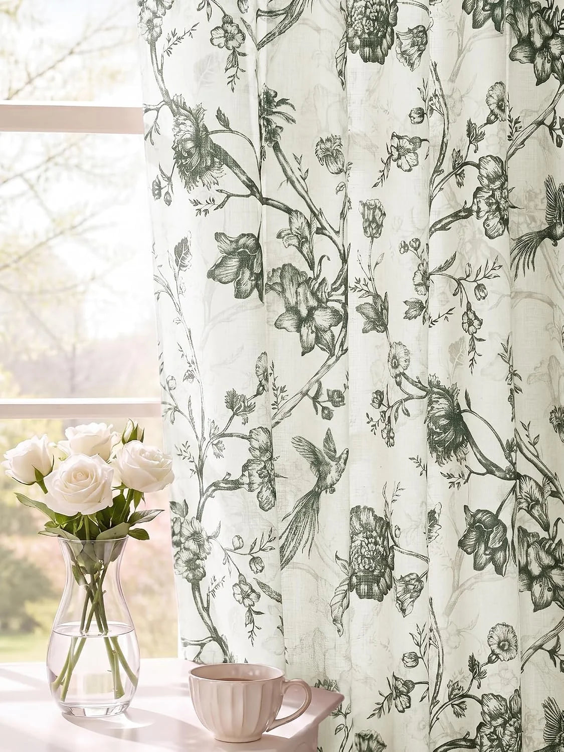 Ivory sheer curtain with black botanical and bird print beside a bright window