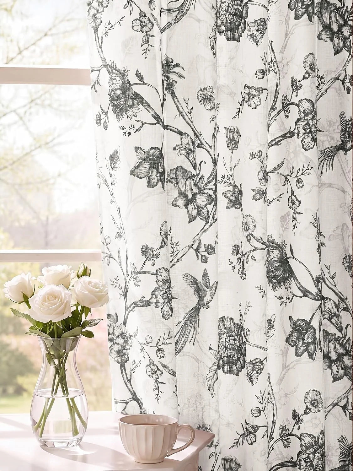Ivory sheer curtain with black botanical and bird print beside a bright window