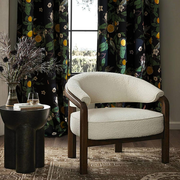 Ivory boucle accent chair with dark wood frame. Black curtains with lemon and bird pattern.