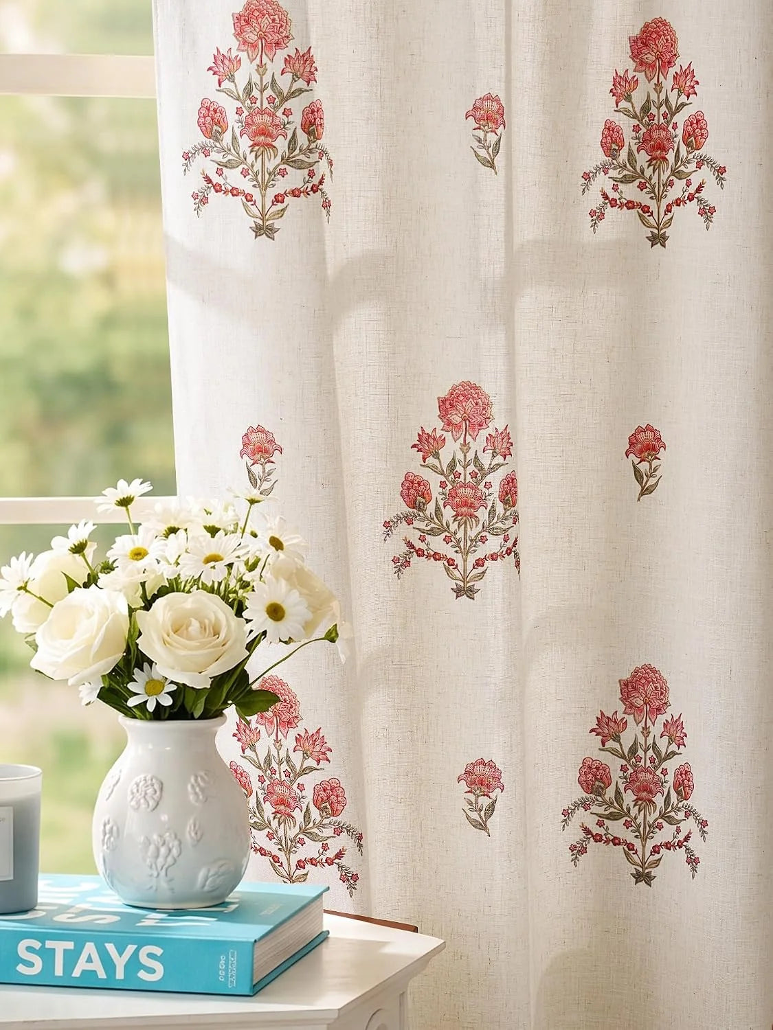 Ivory linen curtain with pink floral print beside a white vase of fresh flowers