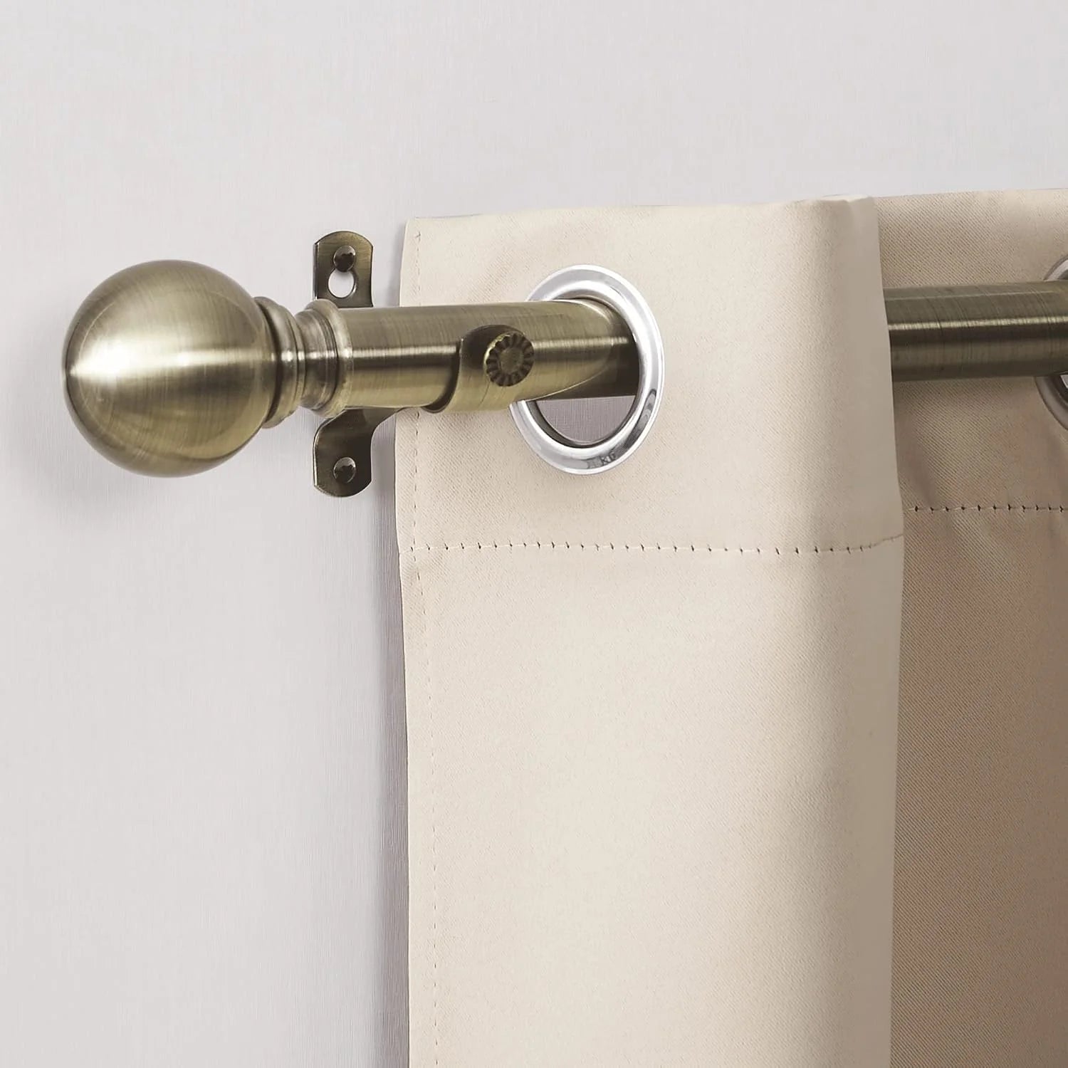 Ivory grommet curtain hanging on an antique brass curtain rod with round finial