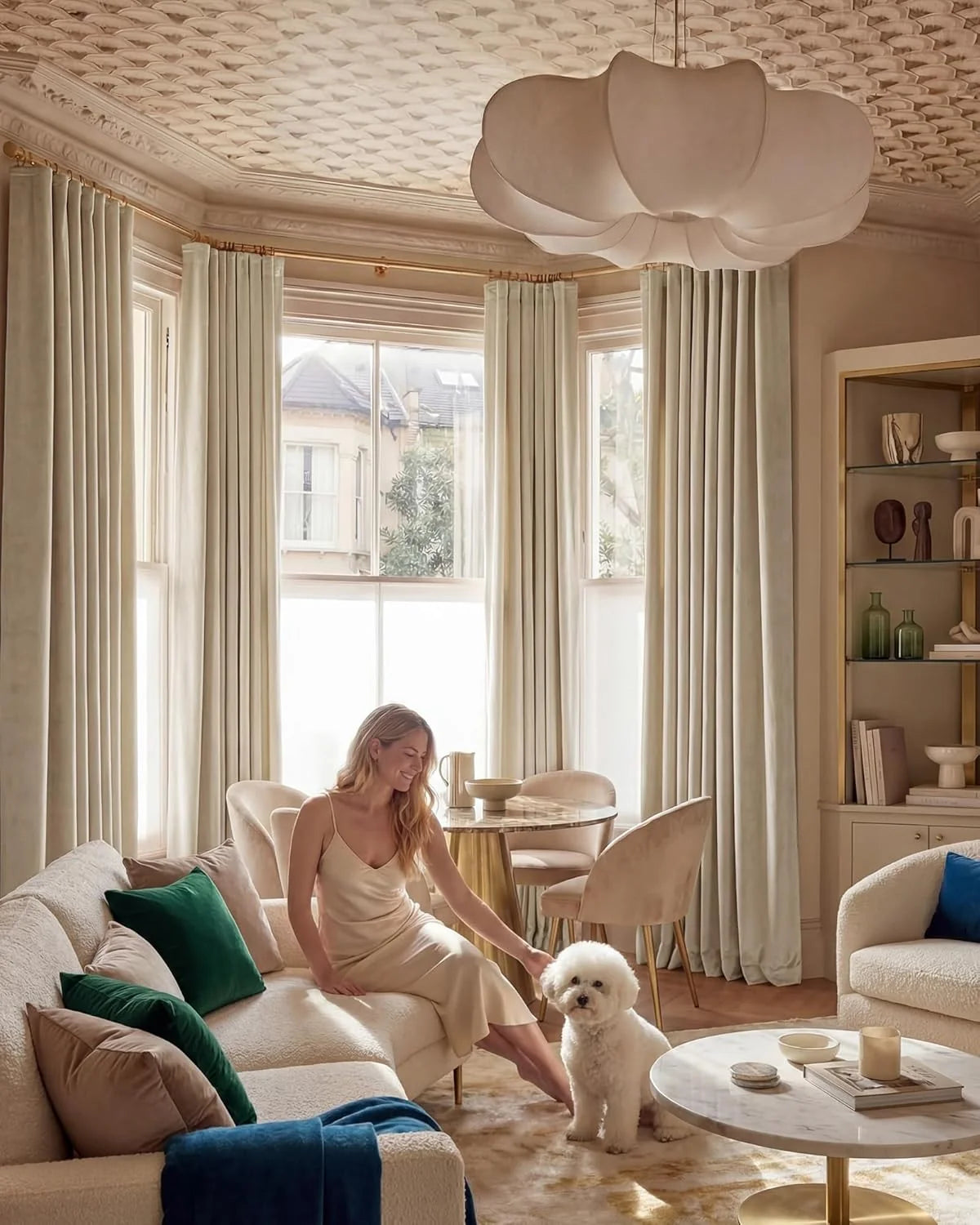 Ivory floor-length curtains in an elegant living room with boucle sofa, marble table, and small white dog