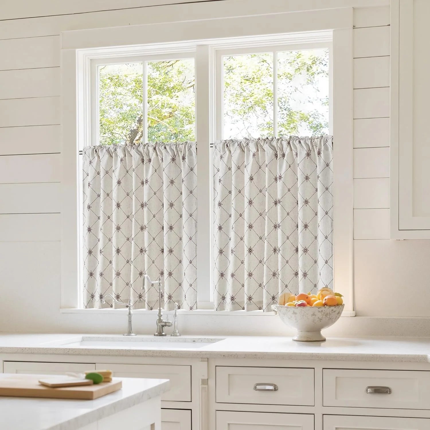 Ivory patterned linen cafe curtains covering a bright kitchen window above the sink